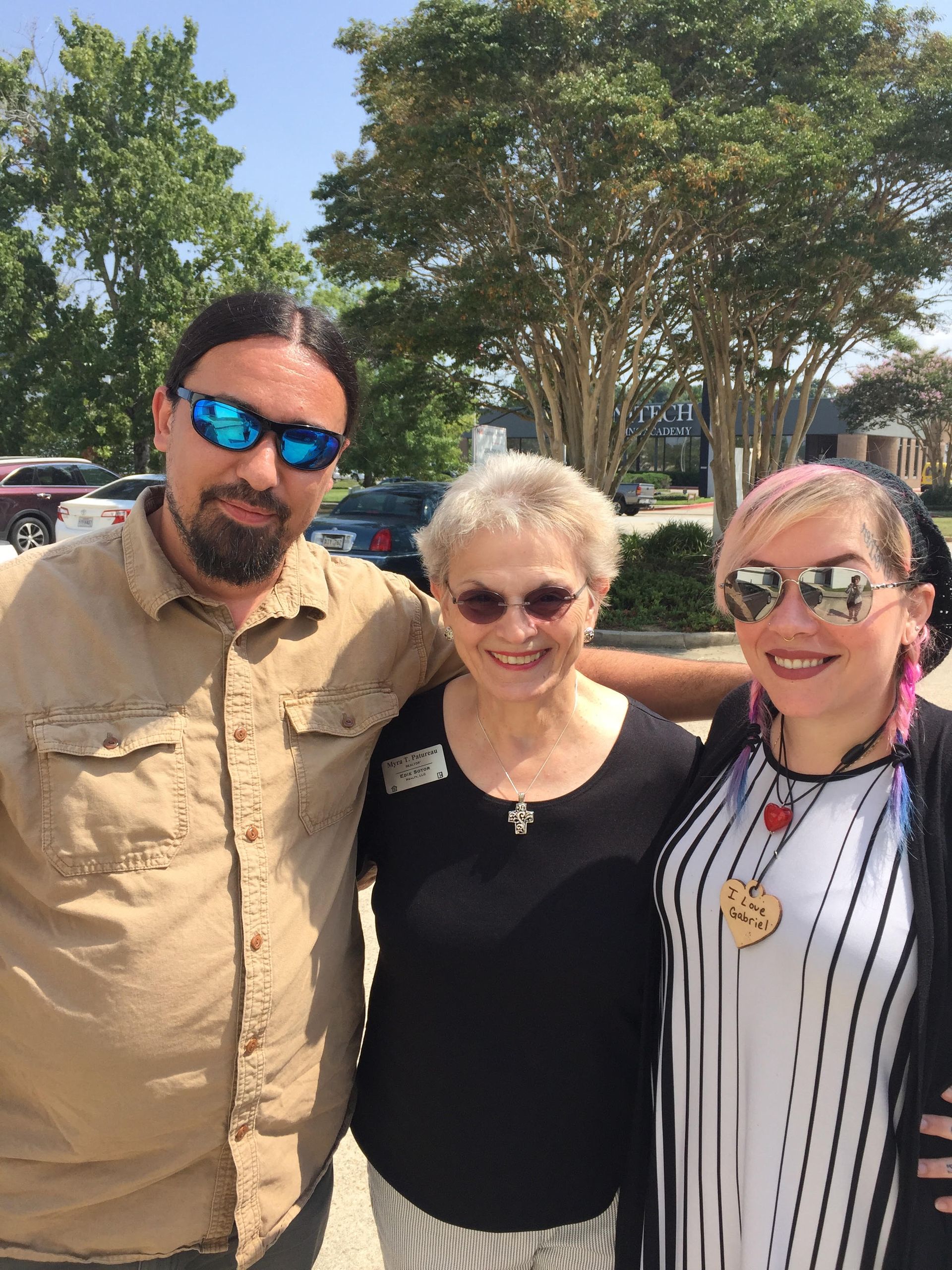 A man and two women are posing for a picture in front of trees.