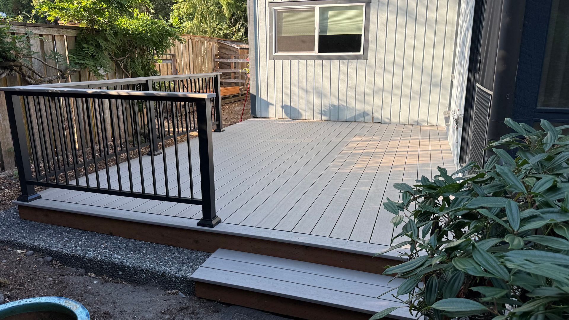 Backyard deck with gray flooring, black railing, and a house wall with a window