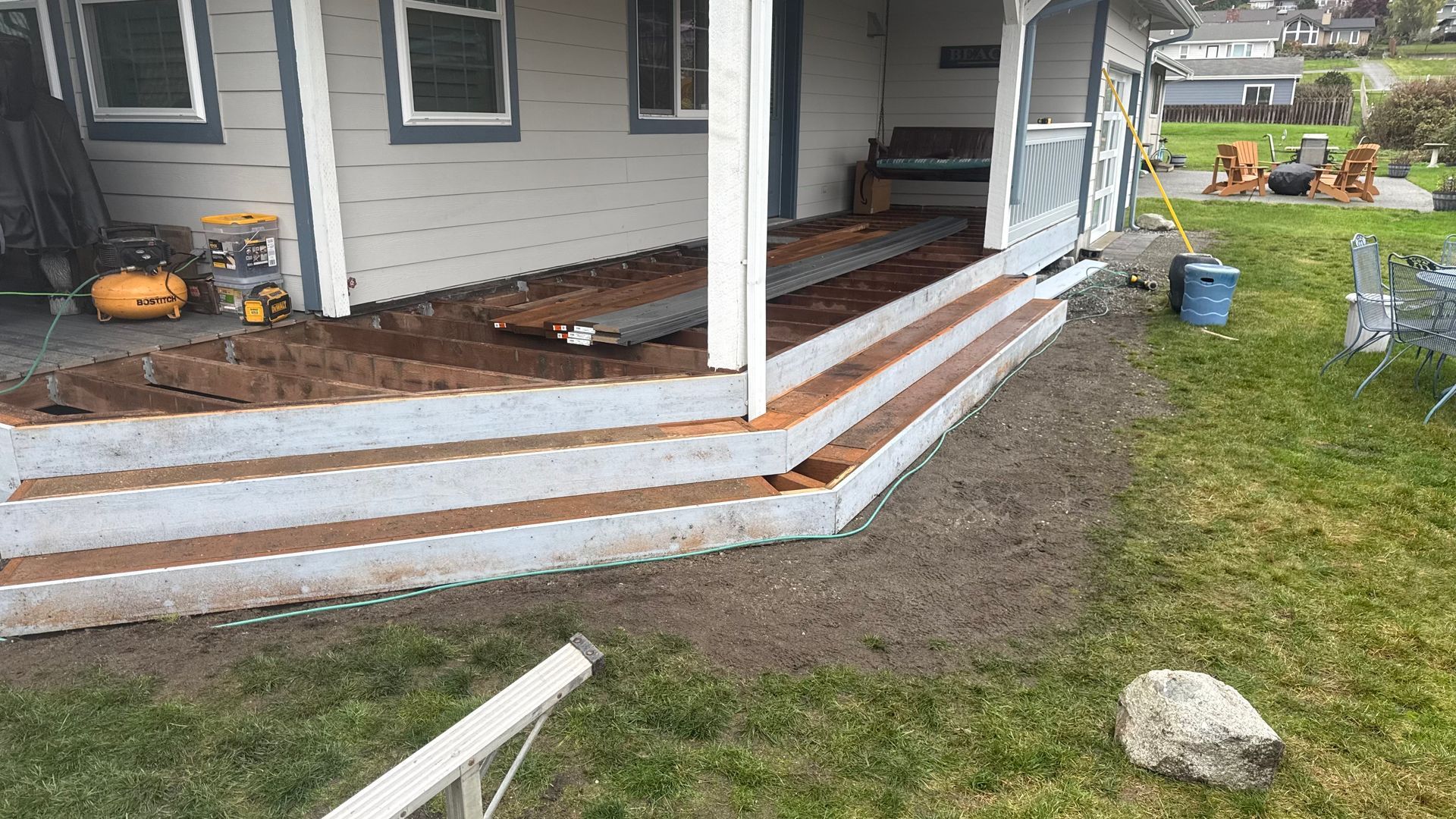 Side of a gray house with a raised porch and fresh dirt landscaping in the yard