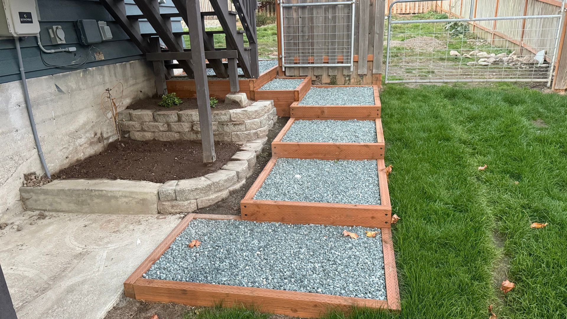 Gravel walkway with wooden borders leading beside a house to a backyard gate and lawn