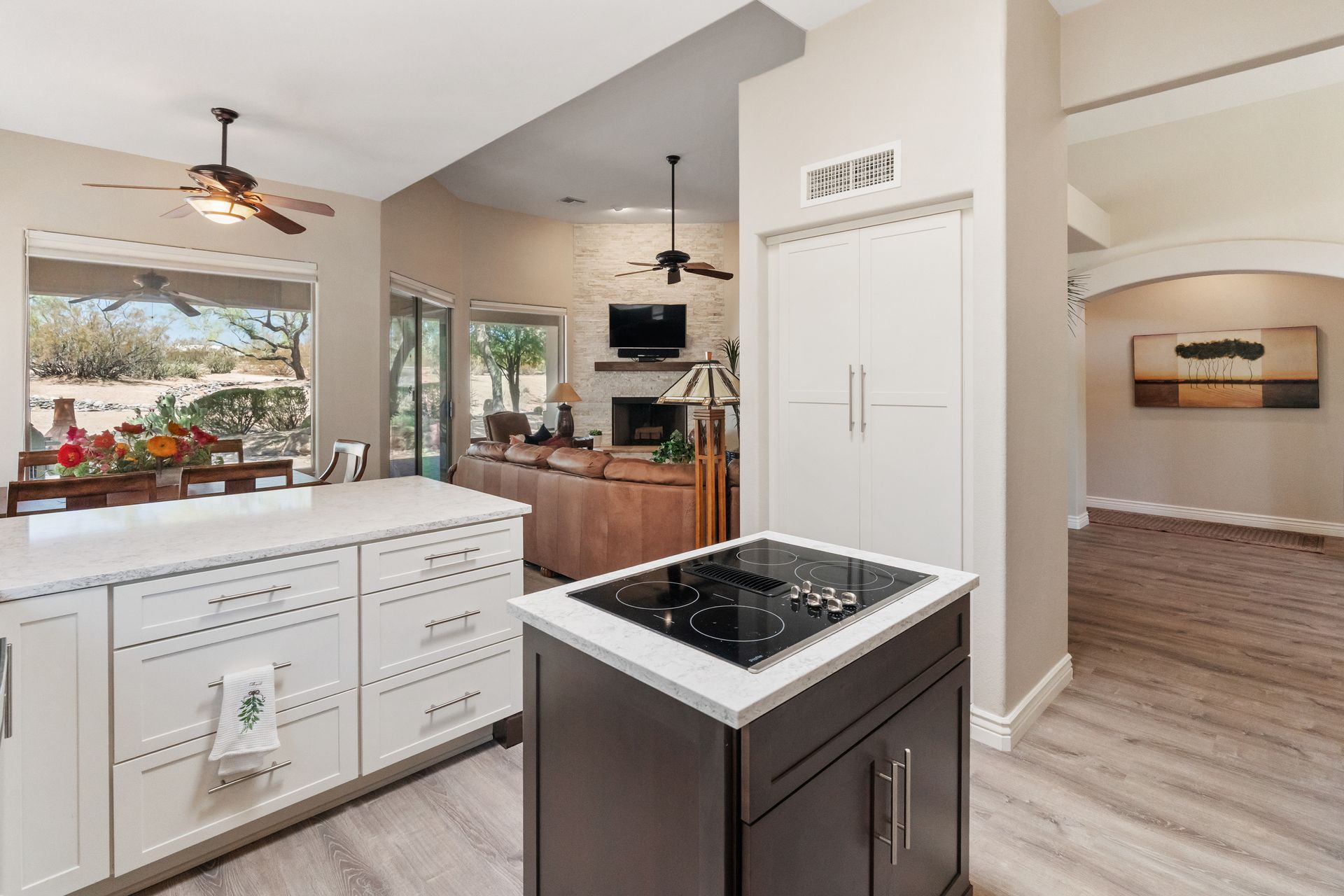 Kitchen with island, white cabinets, stovetop, window view. Neutral tones, modern design, ceiling fans.