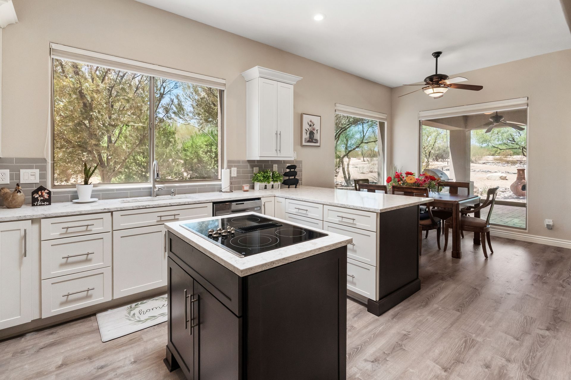 Modern kitchen with white cabinets, dark island with cooktop, and dining area with outdoor view.