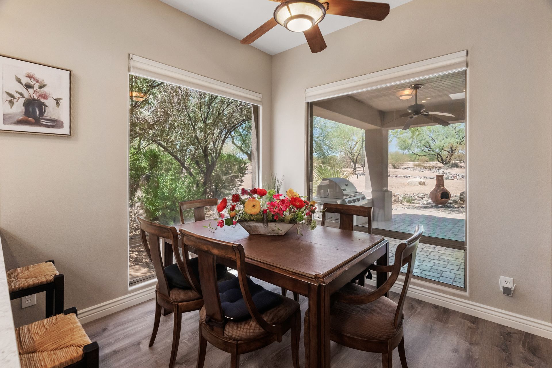 Dining room with table and chairs, windows overlooking outdoor patio and landscaping.