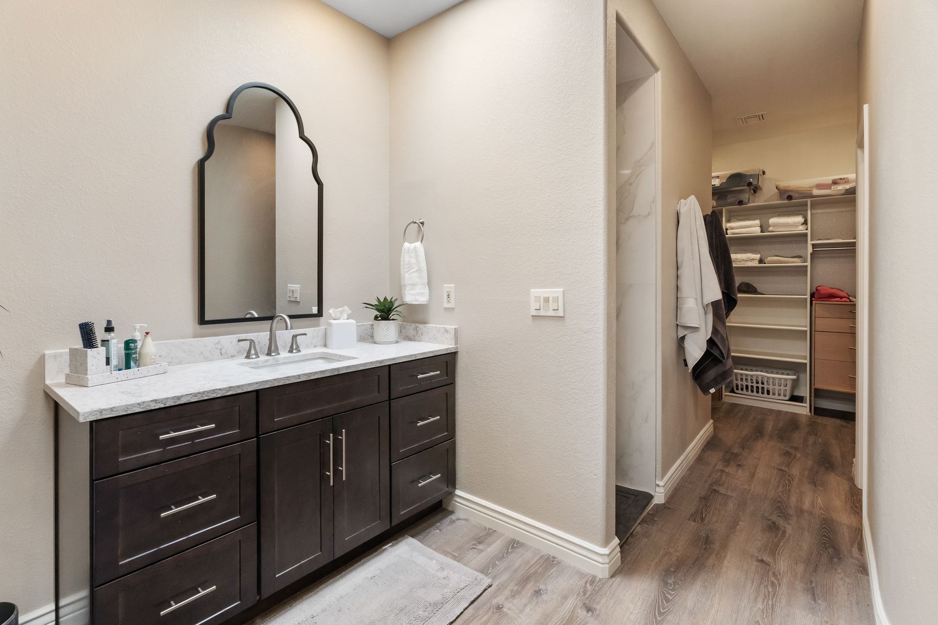Bathroom with dark brown vanity, white countertop, arched mirror, and walk-in closet.