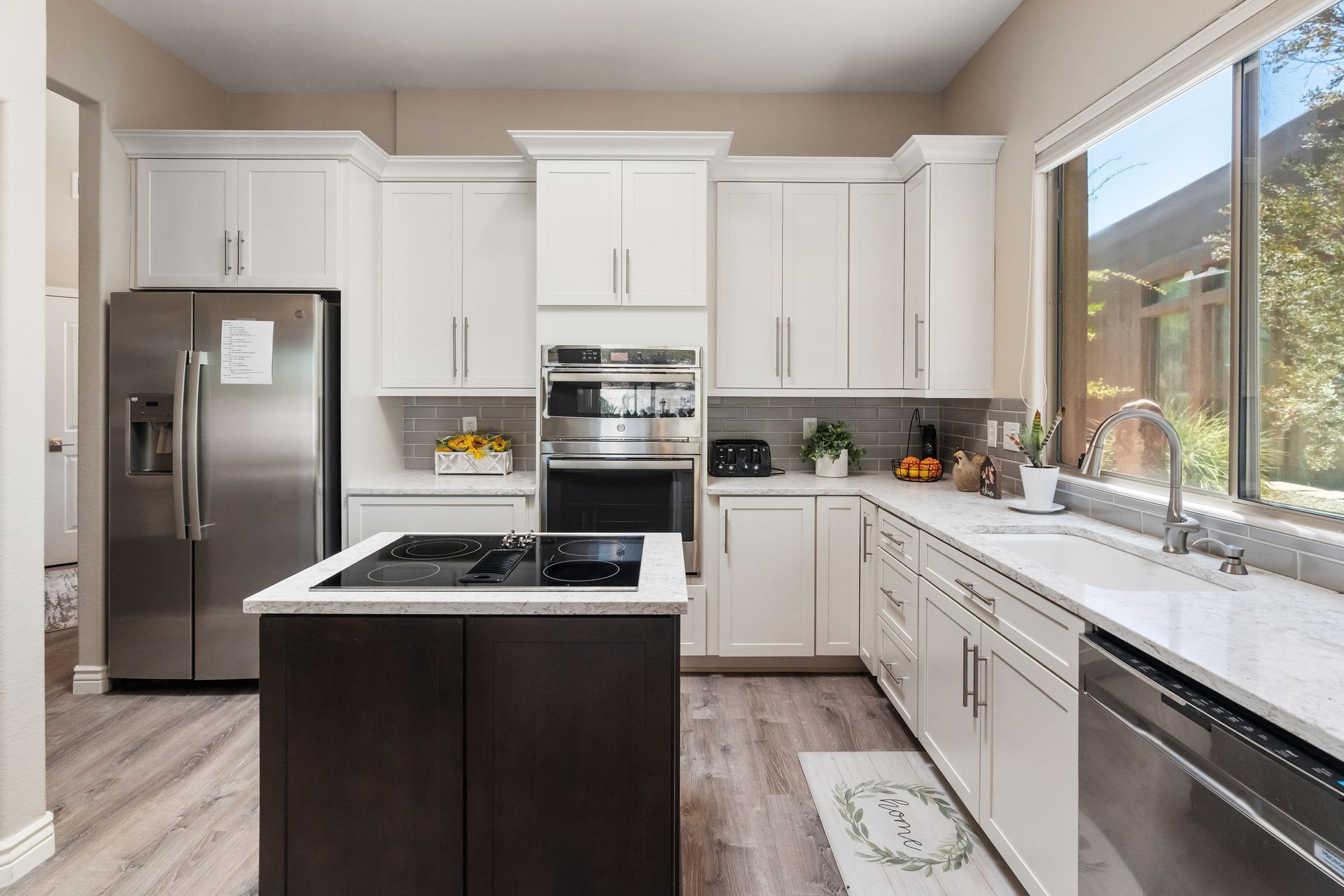 Modern kitchen with white cabinets, stainless steel appliances, dark island, and a large window.
