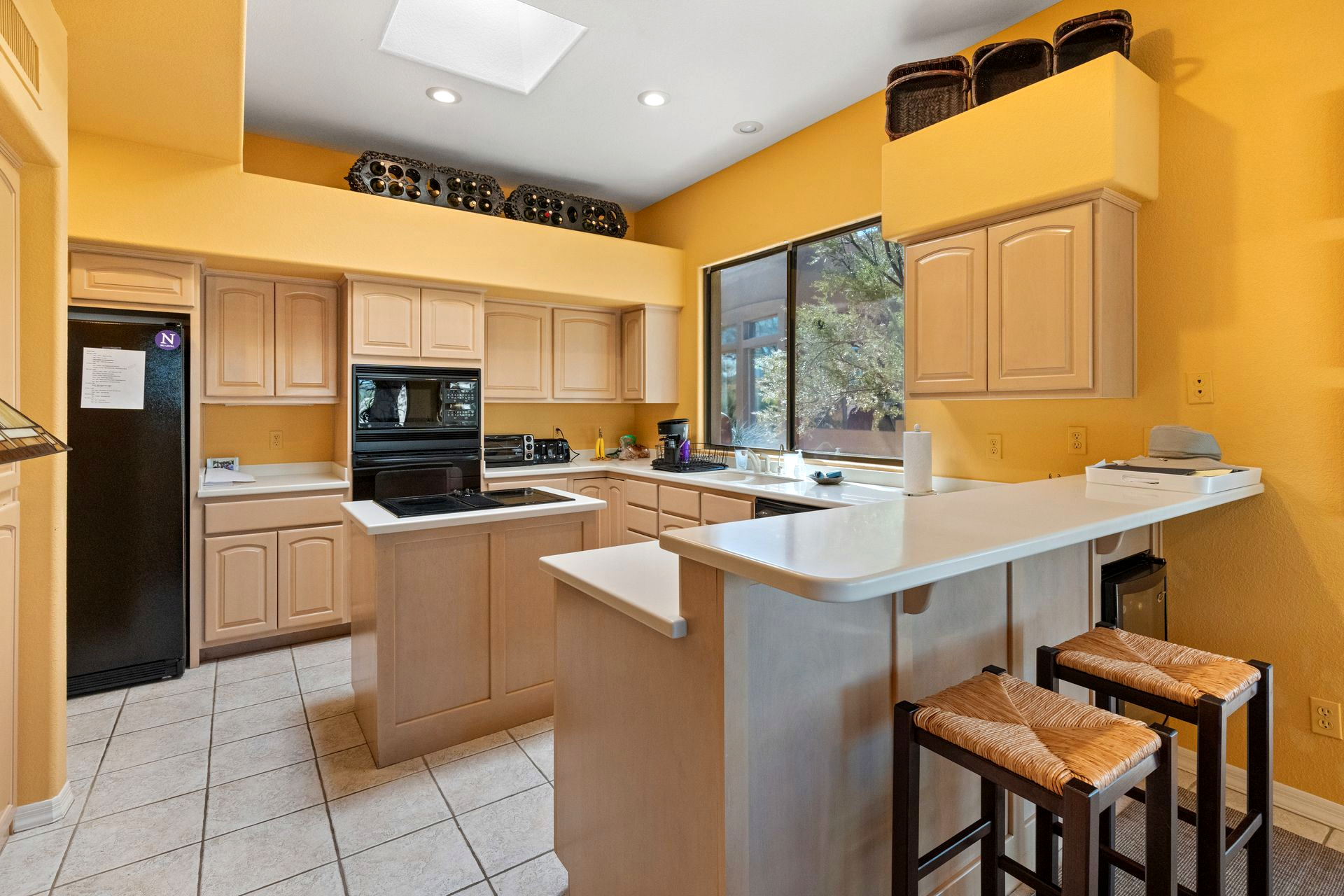 Yellow kitchen with light cabinets, an island, and bar seating.