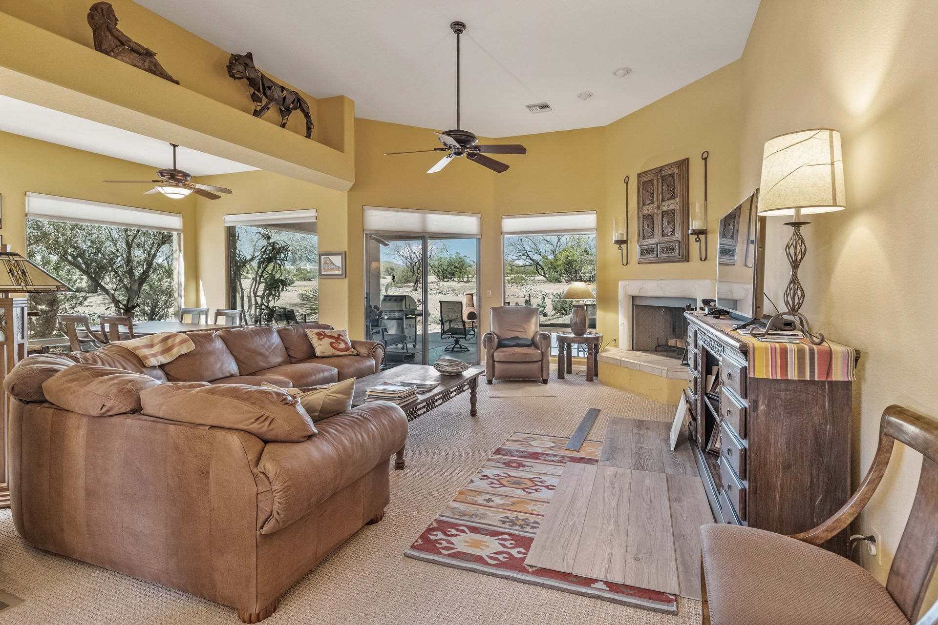 Spacious living room with brown leather sofa, fireplace, and large windows overlooking desert landscape.