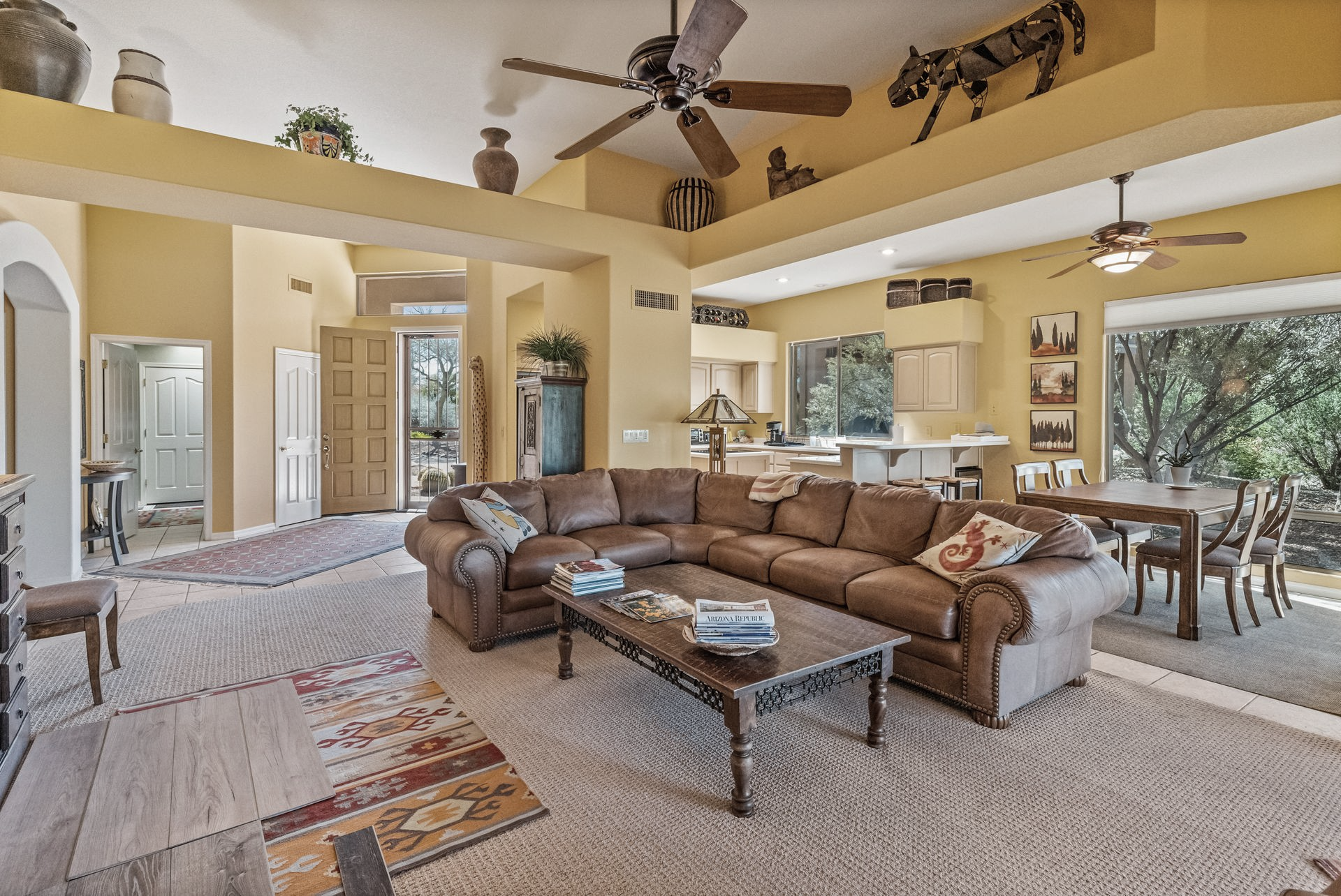 Spacious living room with a brown leather sectional, yellow walls, and a view of trees.