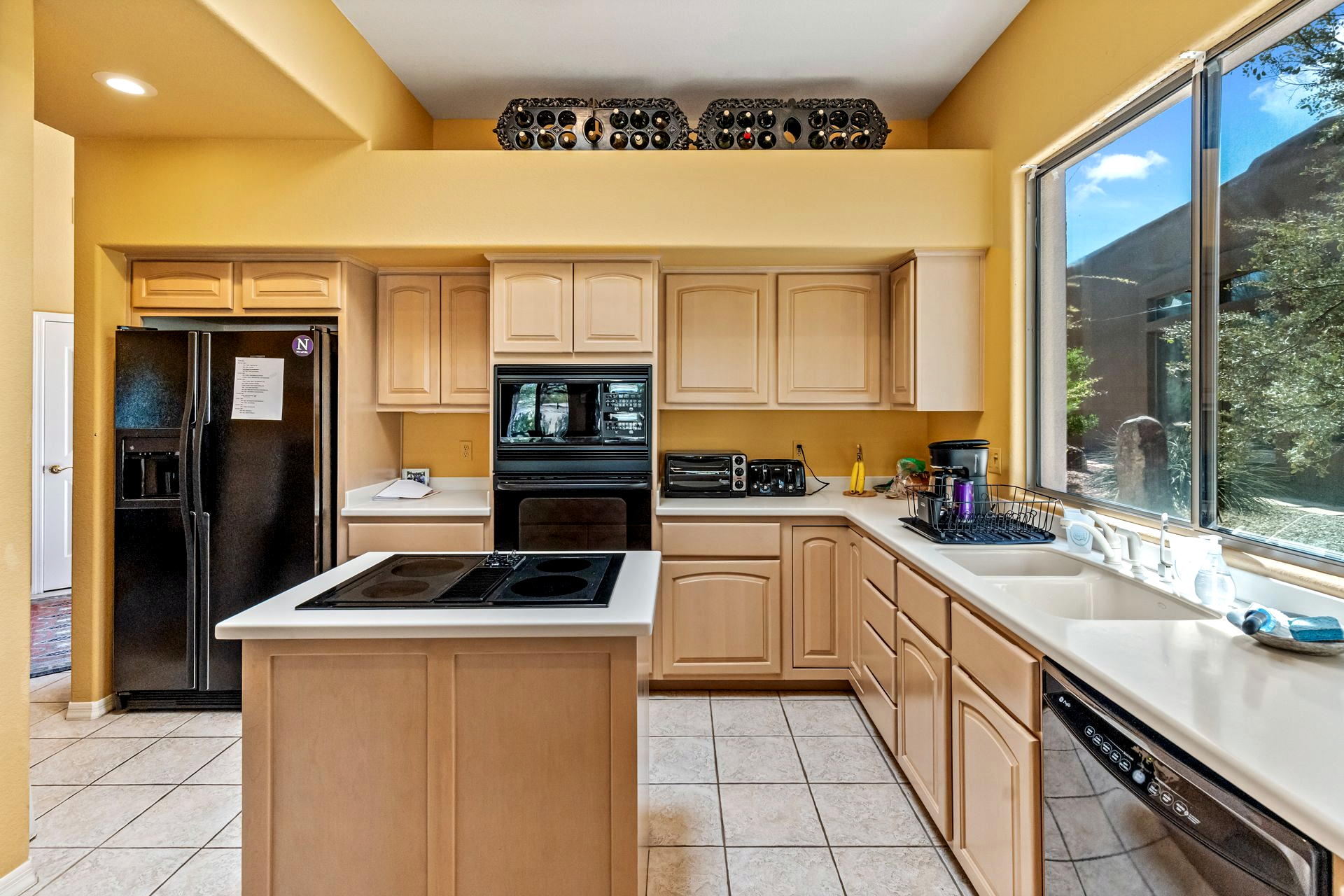 Kitchen with light wood cabinets, black appliances, and yellow walls.