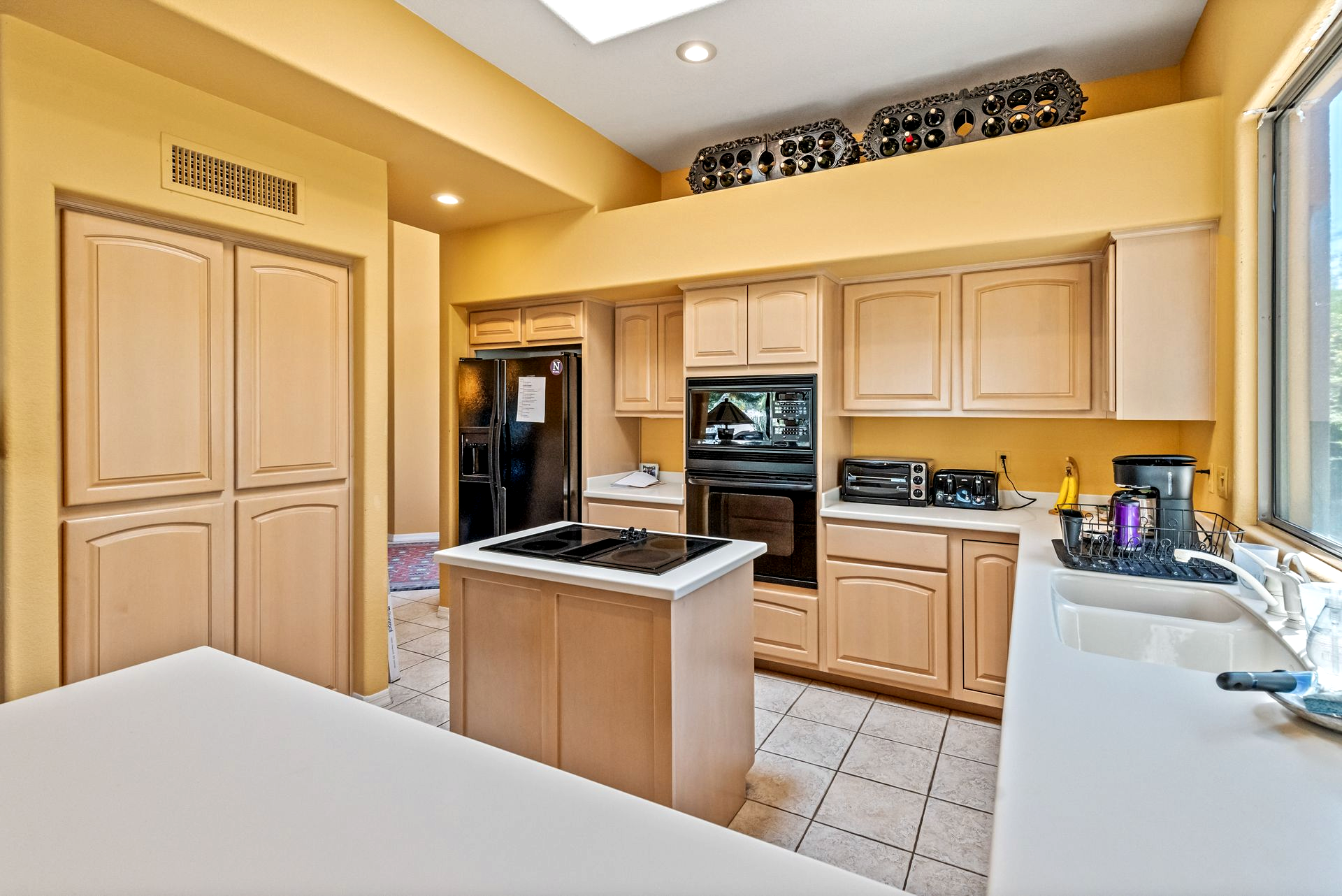 Kitchen with tan cabinets, black appliances, island, and yellow walls.