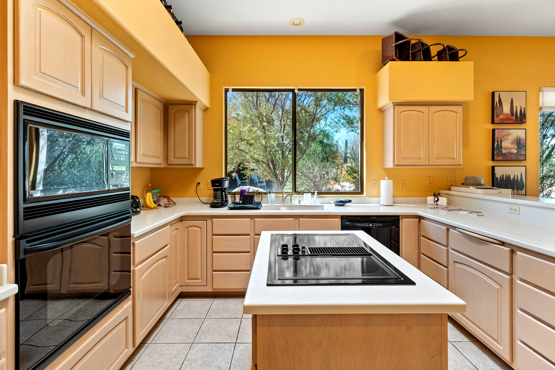 A bright yellow kitchen with light wood cabinets, a black oven, and an island with a stovetop.