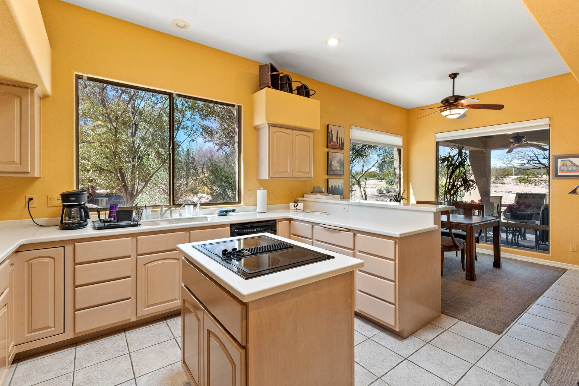 Kitchen with yellow walls, light cabinets, and an island with a stovetop. Windows offer outdoor views.