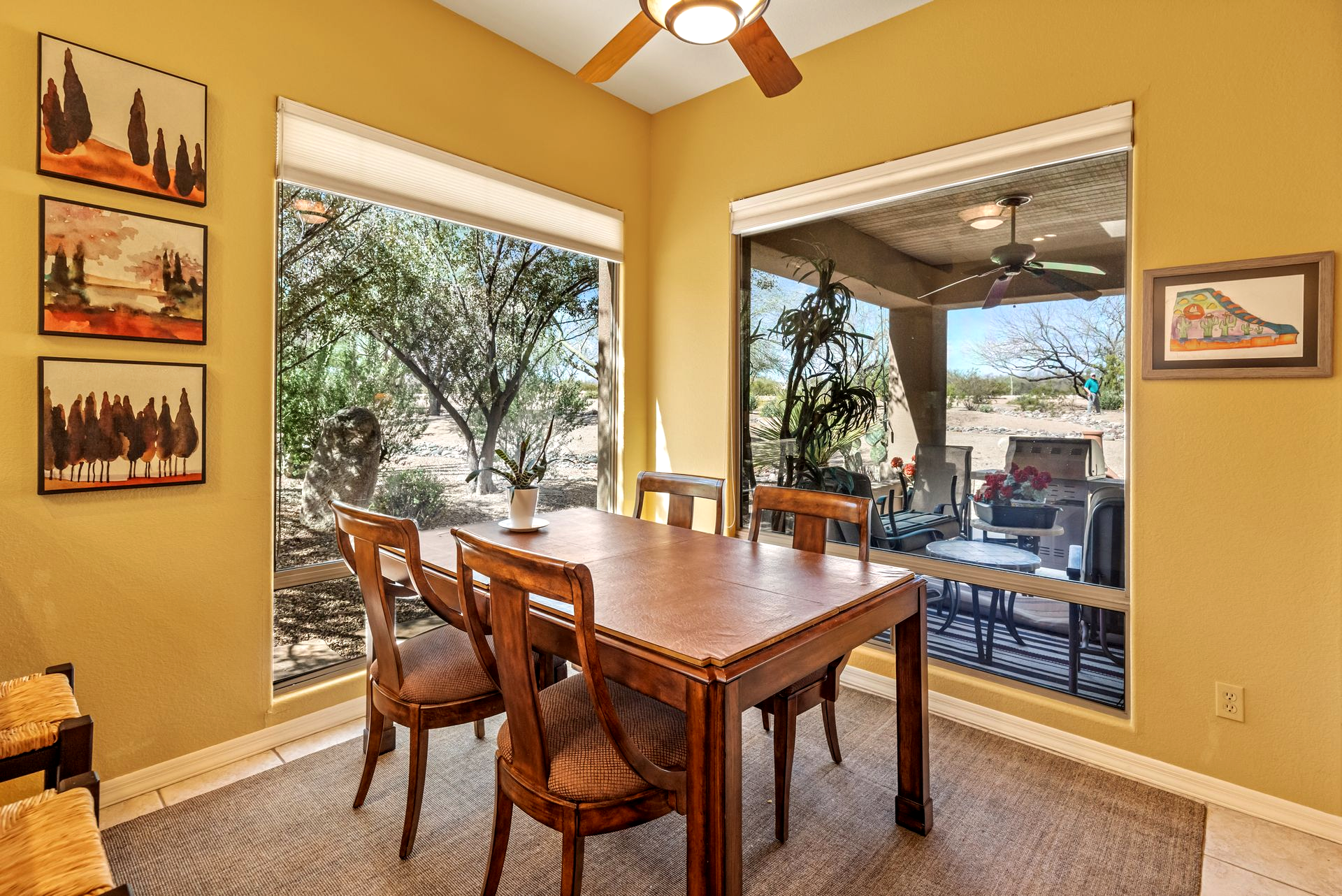 Dining room with wooden table and chairs, large windows overlooking outdoor patio.