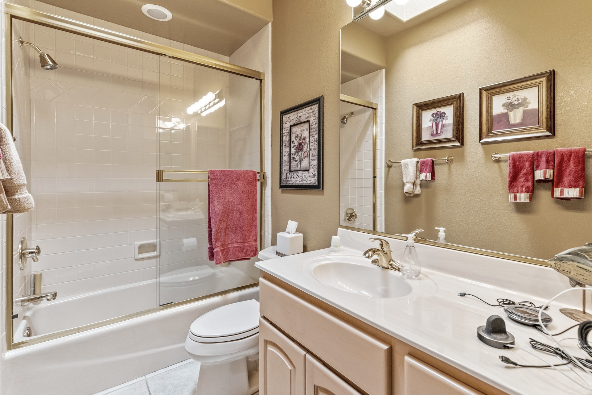 Bathroom with tub, sink, toilet, and gold-framed mirror. Red towels and artwork decorate the light yellow walls.