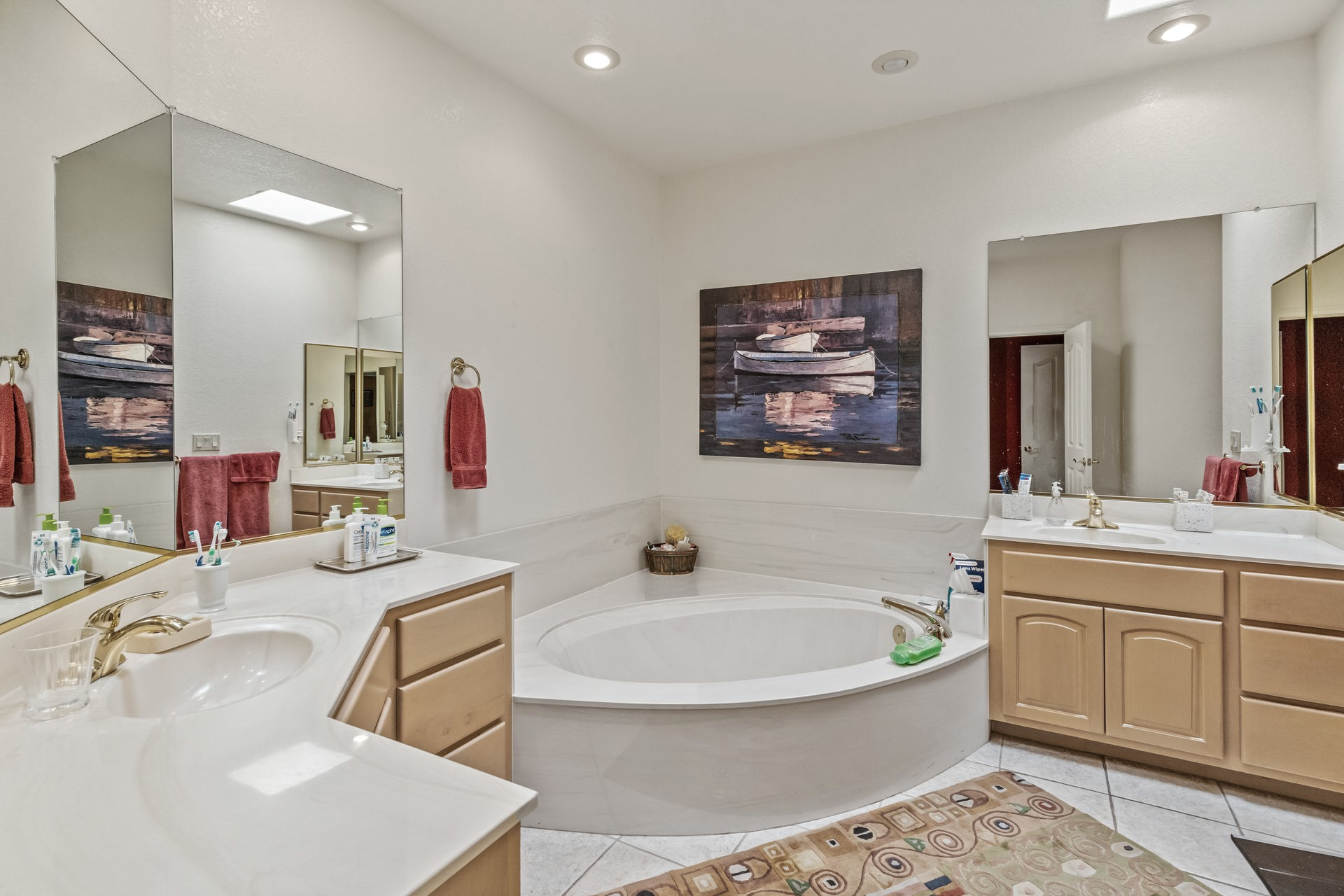 Bathroom with a jacuzzi tub, dual sinks, and large mirrors. The walls are white and the cabinets are light wood.