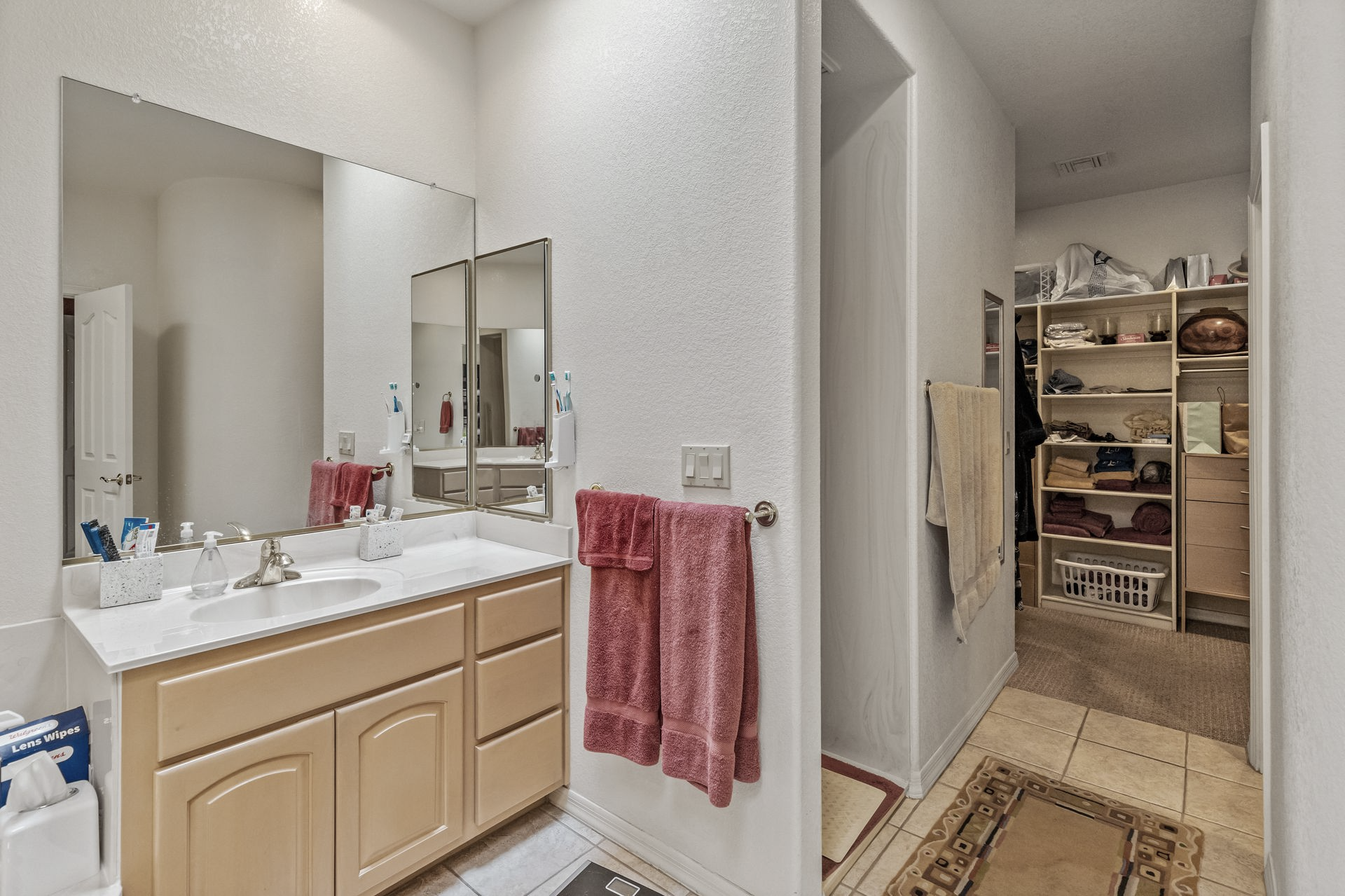 Bathroom with wooden vanity, large mirror, red towels, and a walk-in closet.