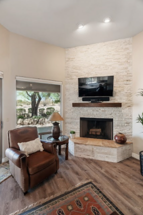 Cozy living room with brick fireplace, brown leather chair, rug, window overlooking a yard.