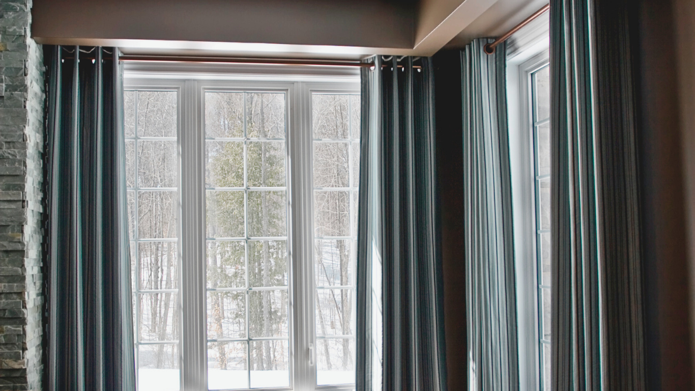 Blue curtains frame a multi-pane window overlooking a snowy, wooded scene.