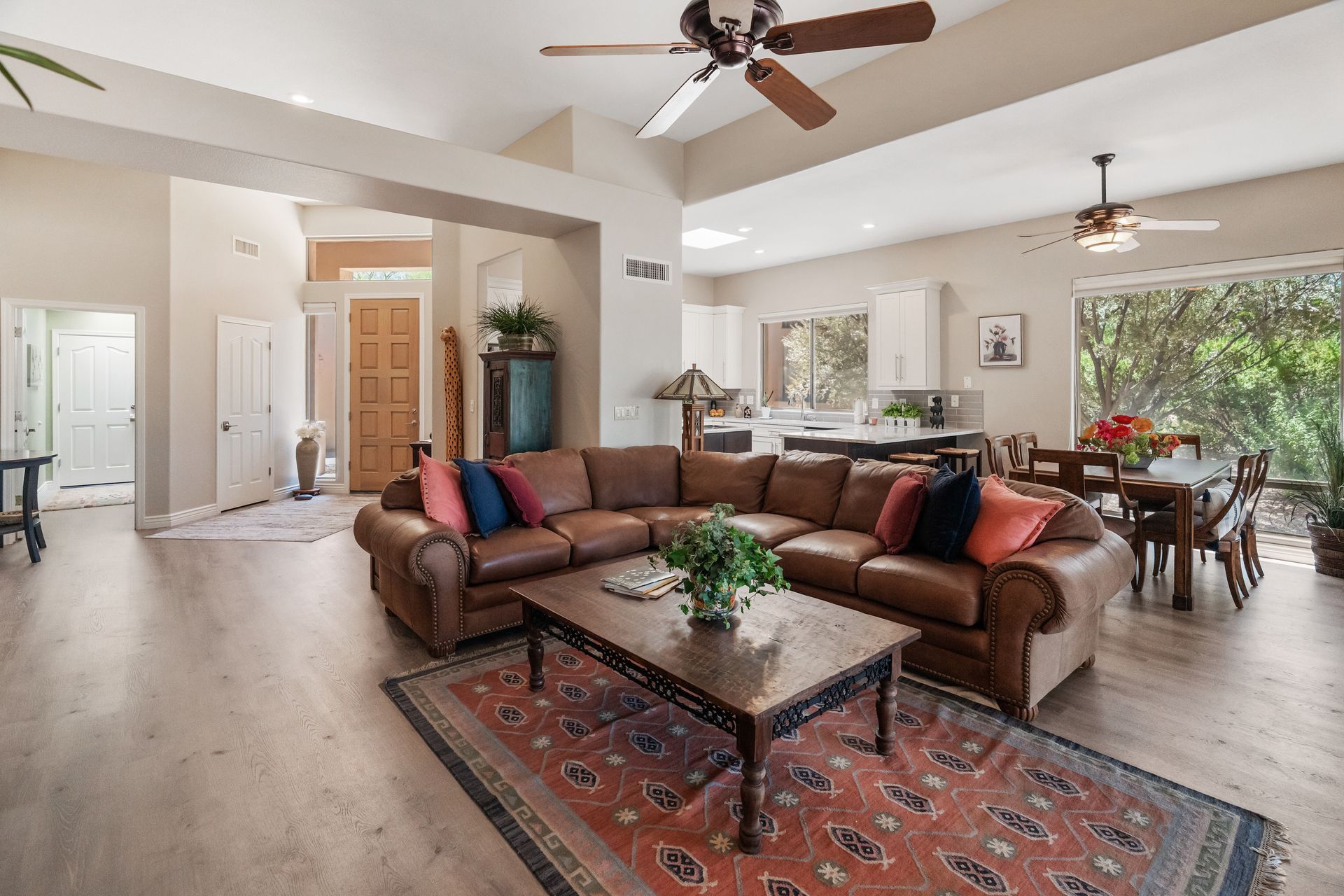 Spacious living room with brown leather sectional, coffee table on patterned rug, dining area, and kitchen.