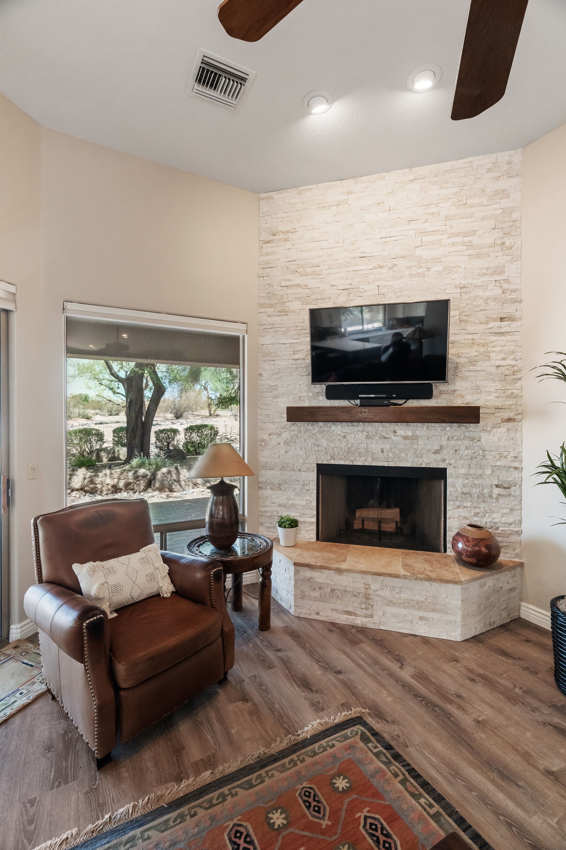 Cozy living room with stone fireplace, large window, leather recliner, and area rug.
