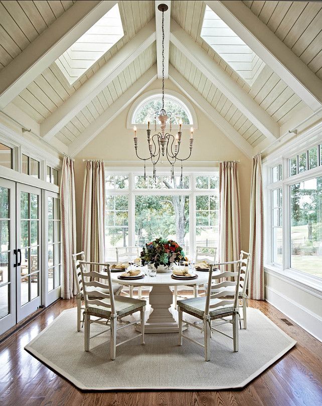 Dining room with round table and six chairs, centered under a chandelier. Skylights and large windows, wood floor.