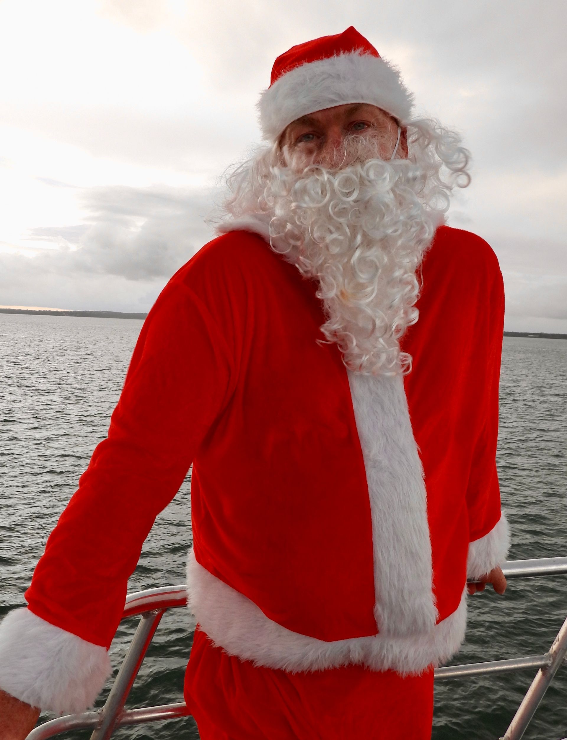 Santa Claus on a boat, wearing red suit and hat, white beard, looking forward, cloudy sky — Costumes Galore In Maroochydore, QLD