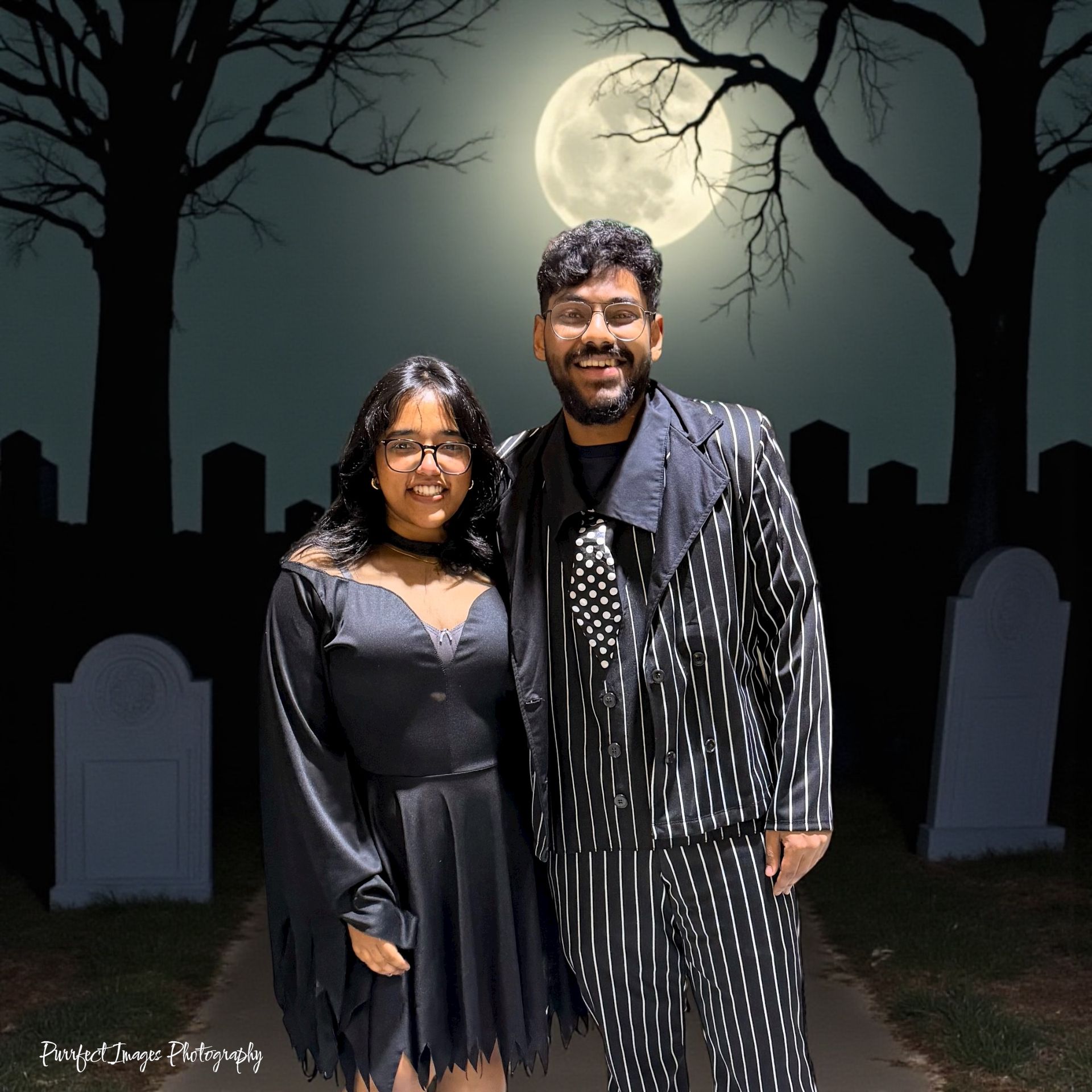 Couple in Halloween costumes posing in front of a graveyard with a full moon.