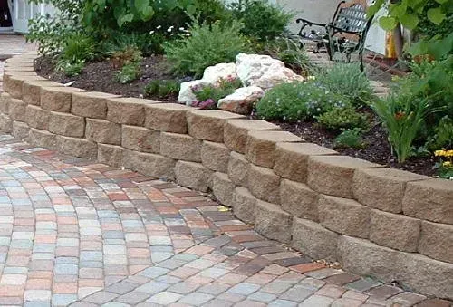 A brick walkway with a stone wall and a bench in the background