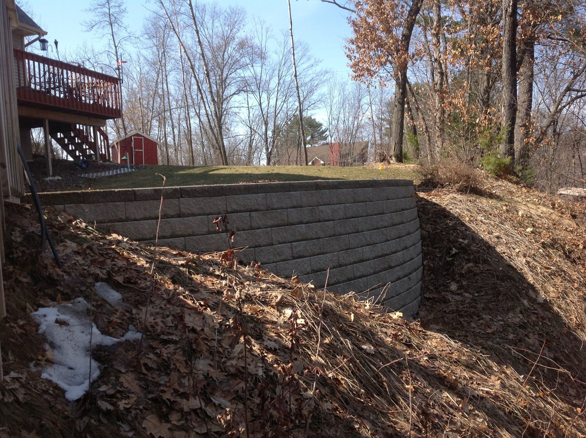 A large brick wall is sitting on top of a hill next to a house.
