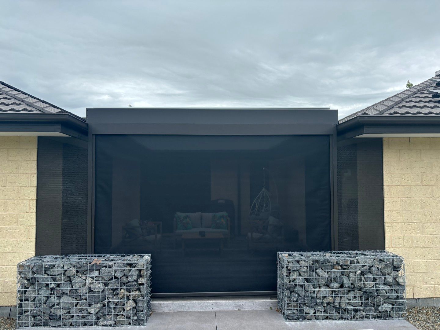 A house with a screened in porch and two rock planters in front of it.