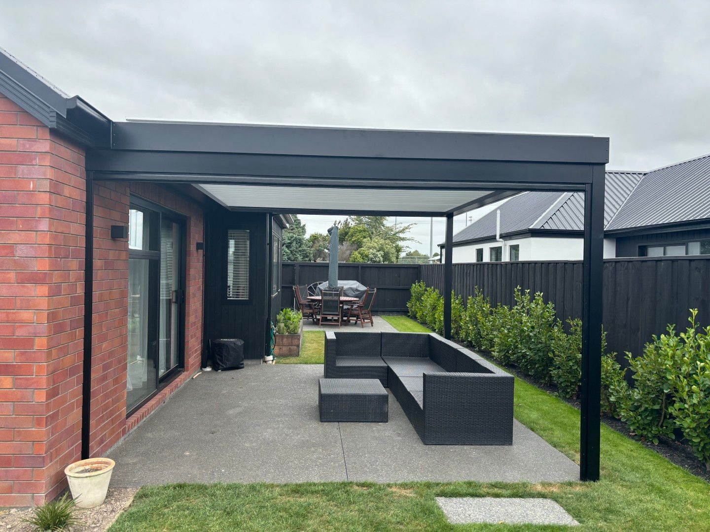 A patio with a couch and a table under a pergola in the backyard of a house.