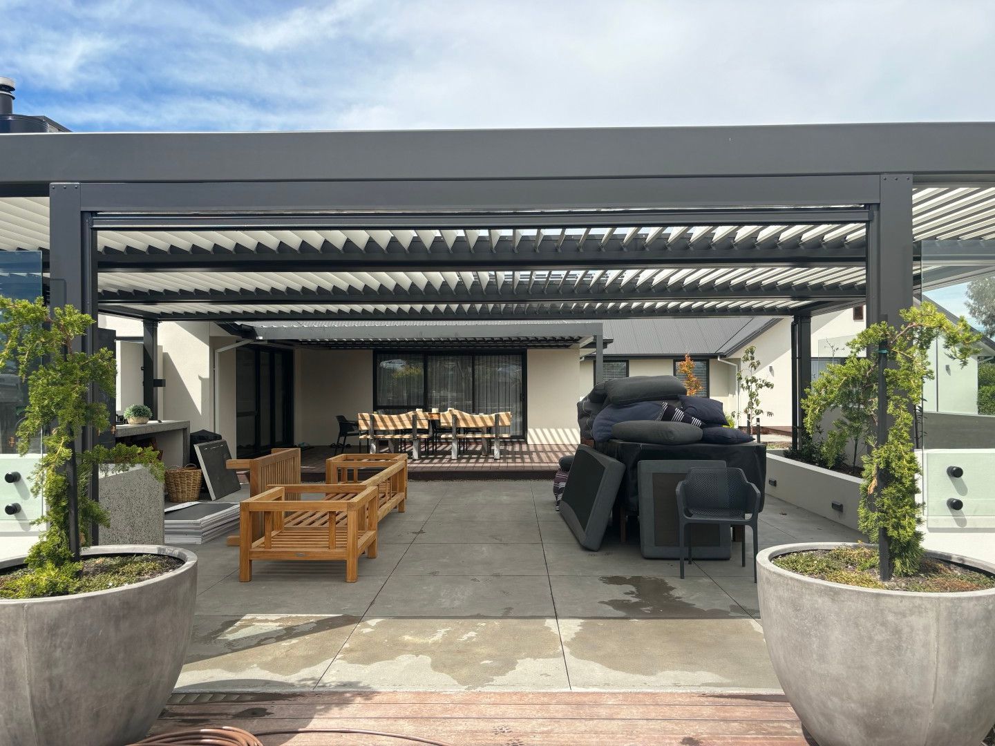 A patio with a pergola and a lot of furniture and potted plants.