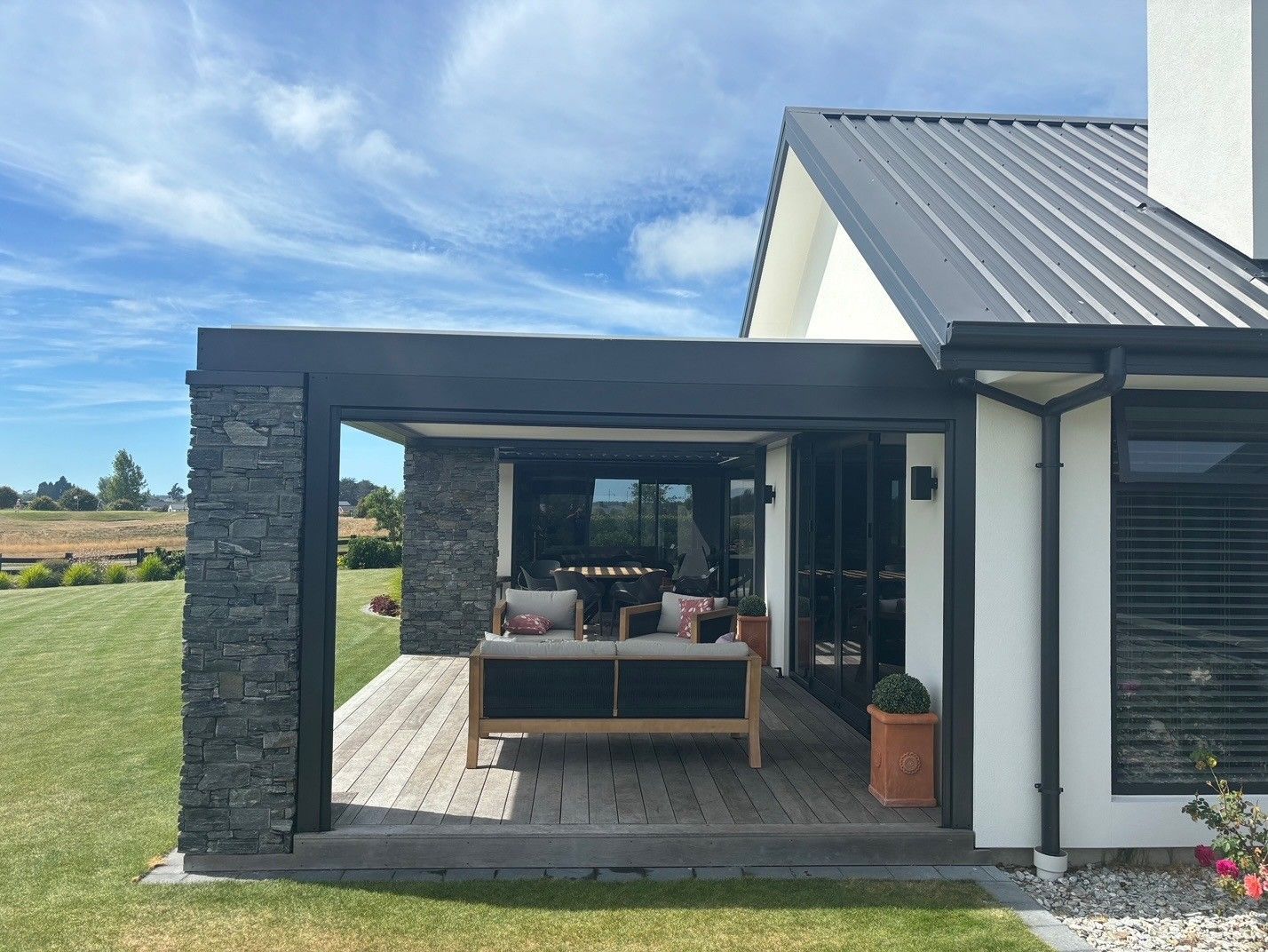 A white house with a black roof and a patio with a couch and chairs on it.