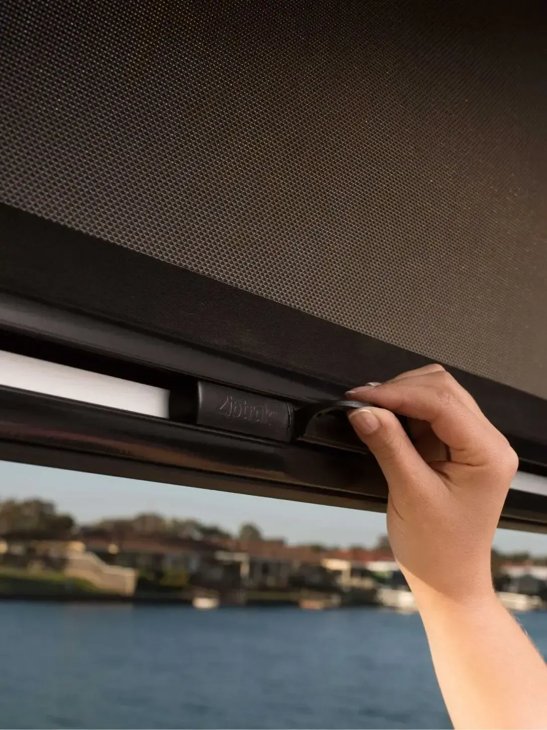 A person 's hand is reaching out to open a window with a view of the water.