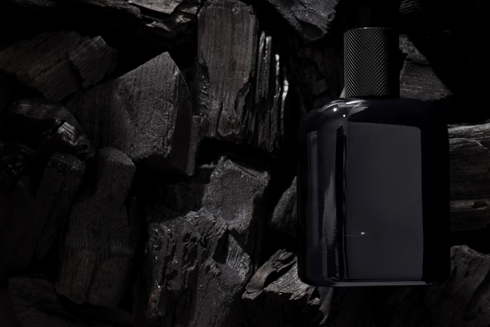 Frasco de perfume negro sobre un lecho de carbón oscuro.