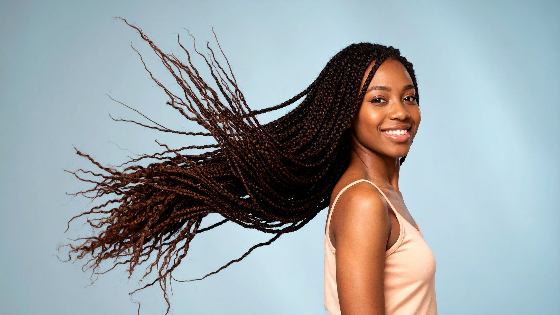 Smiling woman with long braids flowing back against a light blue background
