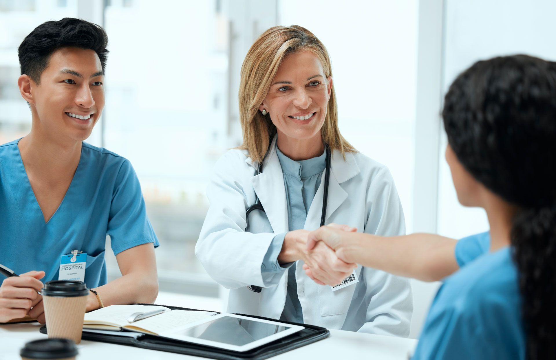 Three medical professionals, one shaking hands with a patient, all smiling, in a bright office.
