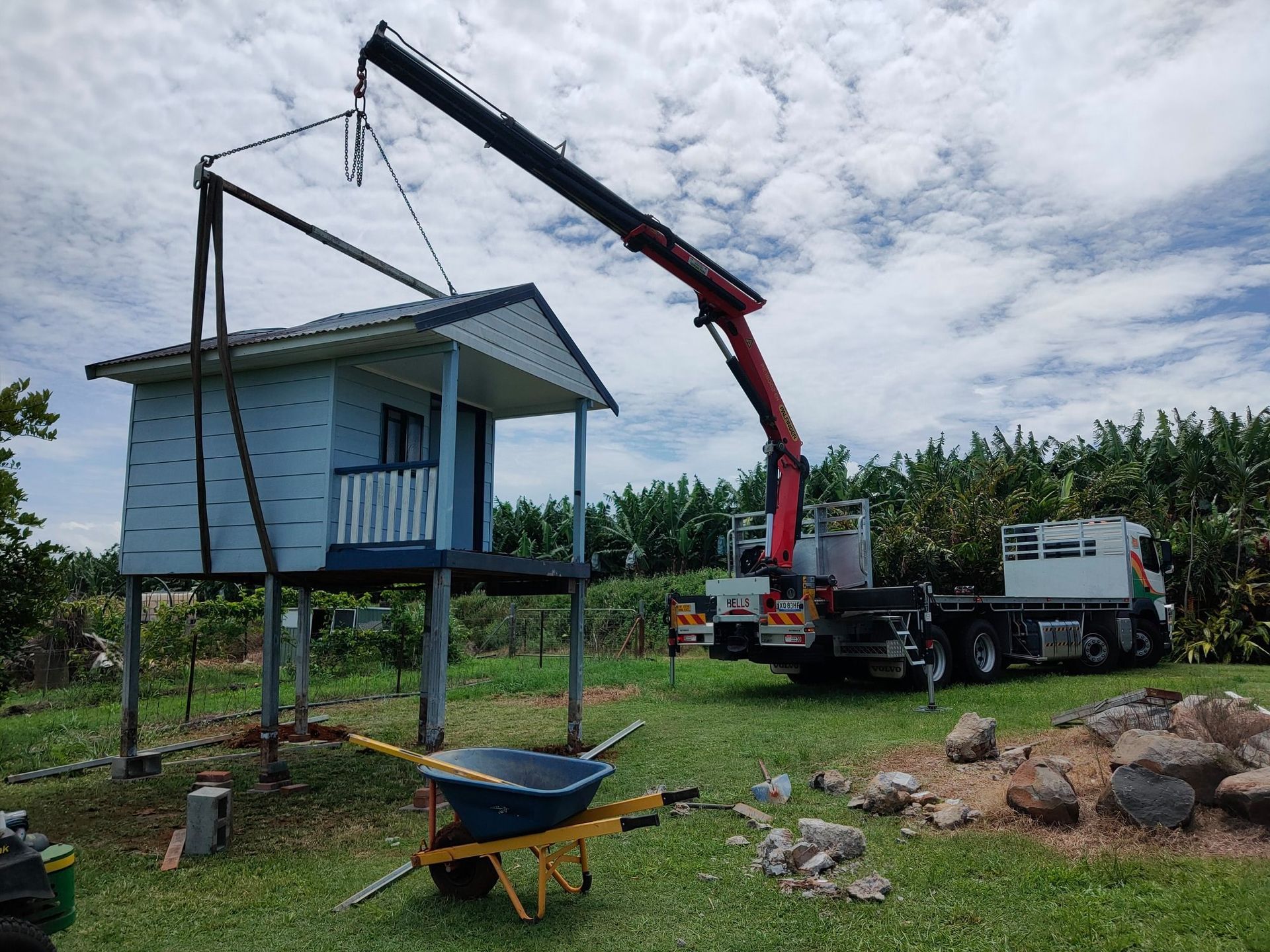 Crane lifting a small blue house on stilts beside a truck — Bell's Carrying & Crane Hire Service Pty Ltd in Atherton, QLD
