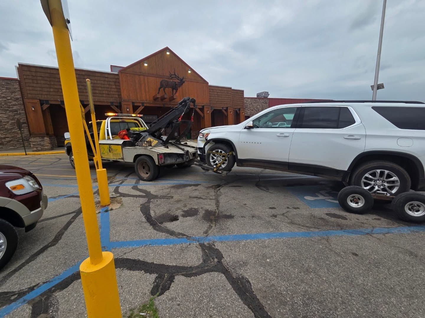 A white SUV being towed away from a building with a rustic facade by a yellow tow truck.
