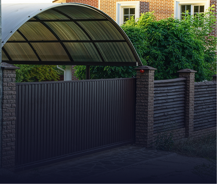 Brown sliding gate with a carport, set against a brick house and greenery.