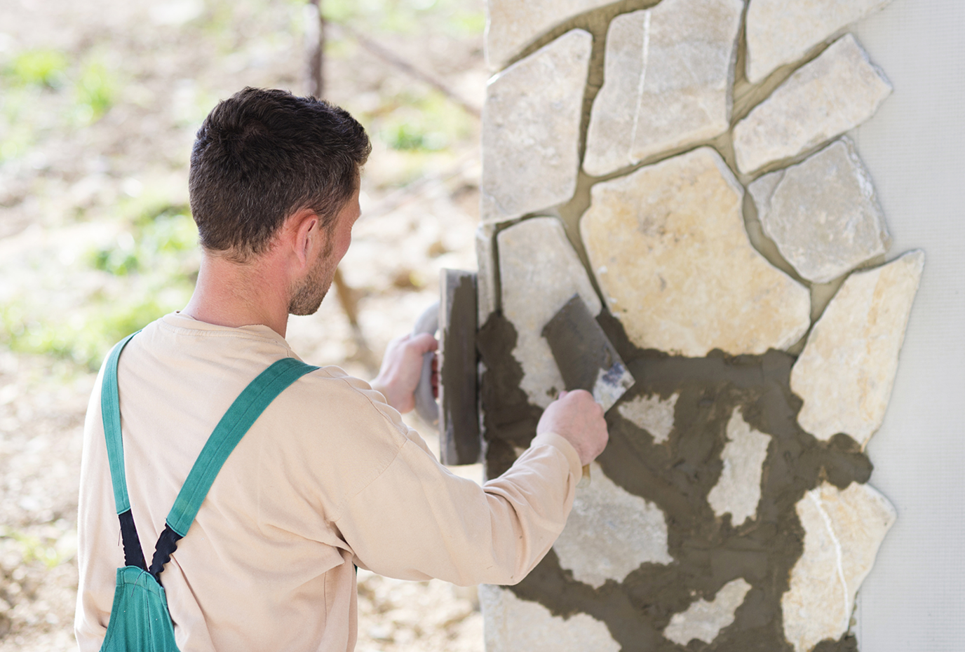 Man applying mortar to a stone wall with a trowel, outdoors.
