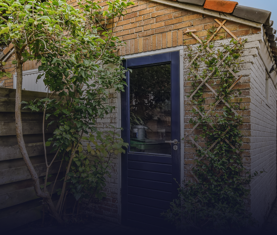 Brick and white shed with a blue door, surrounded by greenery.