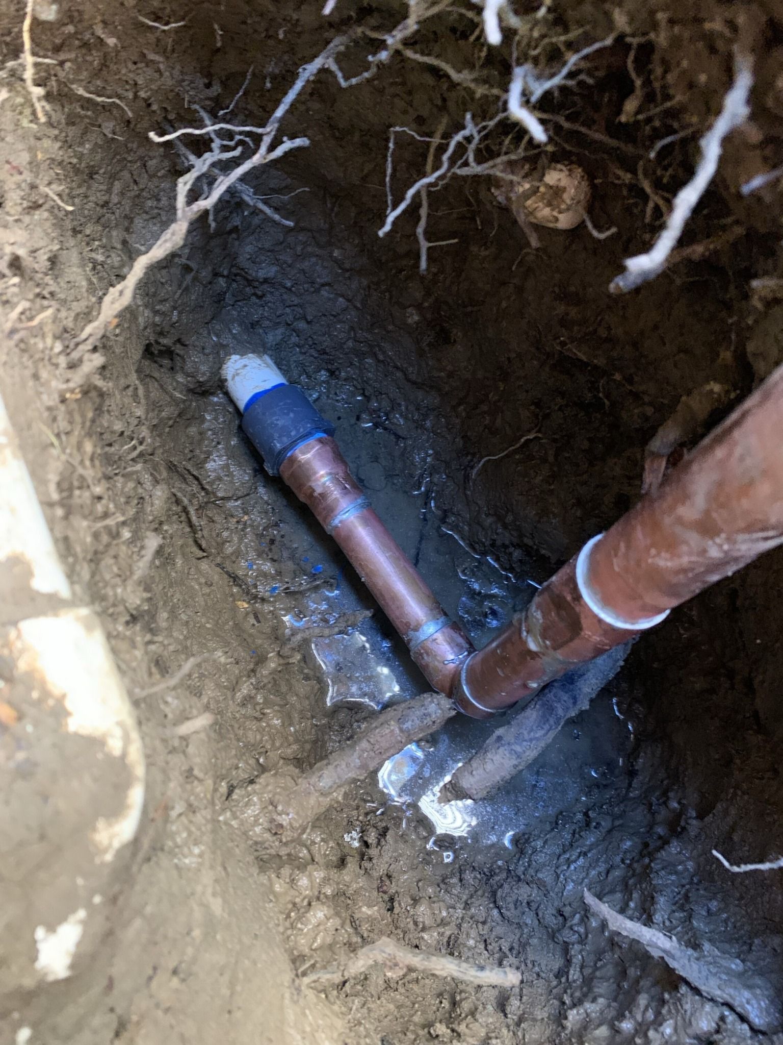 Copper pipes exposed in a ditch, with one pipe joined by a blue fitting and tape.