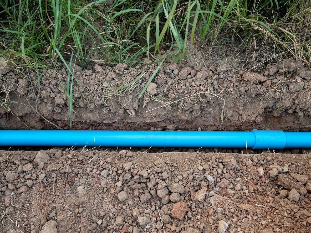 Blue PVC pipe in a trench of brown soil, next to grass.