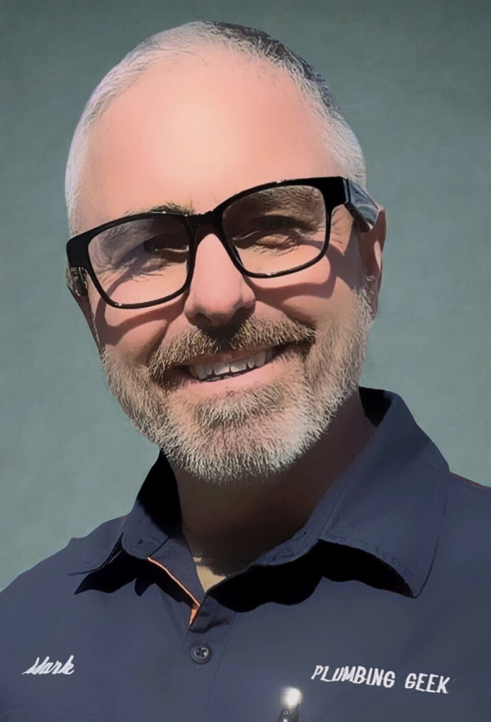 Man with glasses, smiling, wearing a navy blue shirt that says 