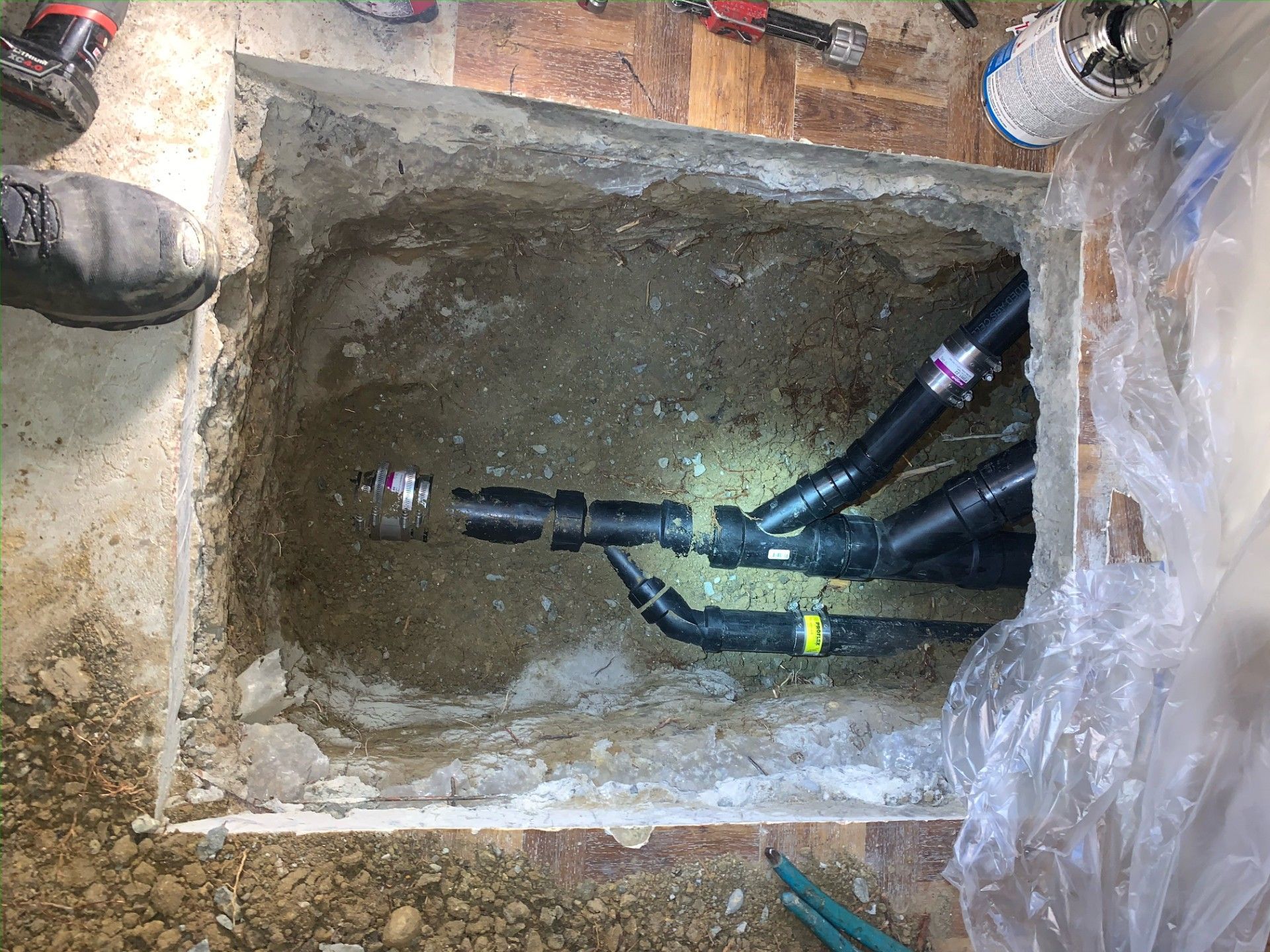 Open excavation showing black plumbing pipes connected, inside a concrete floor.