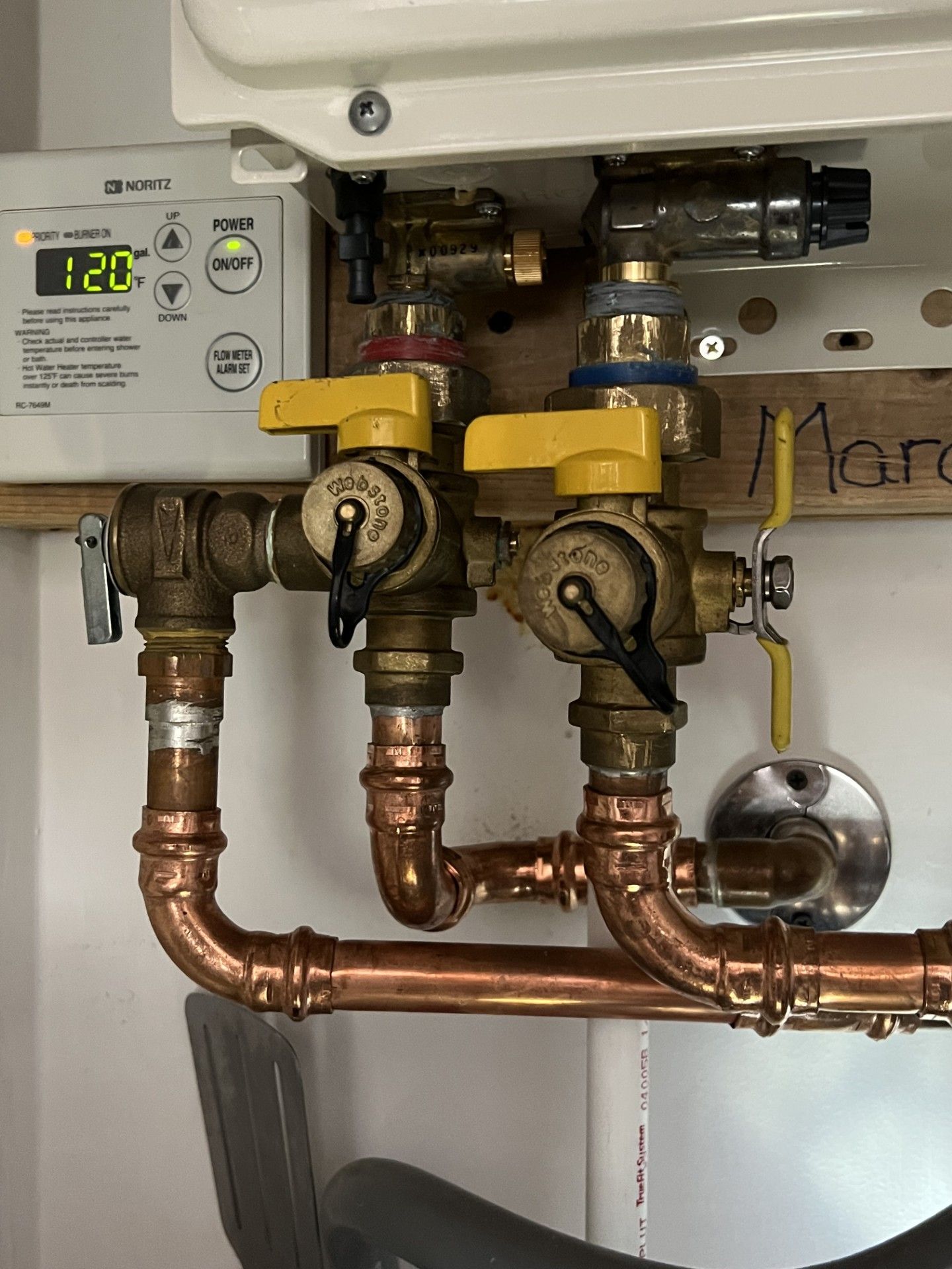 Copper pipes and valves connected to a white wall-mounted boiler with yellow and blue handles.