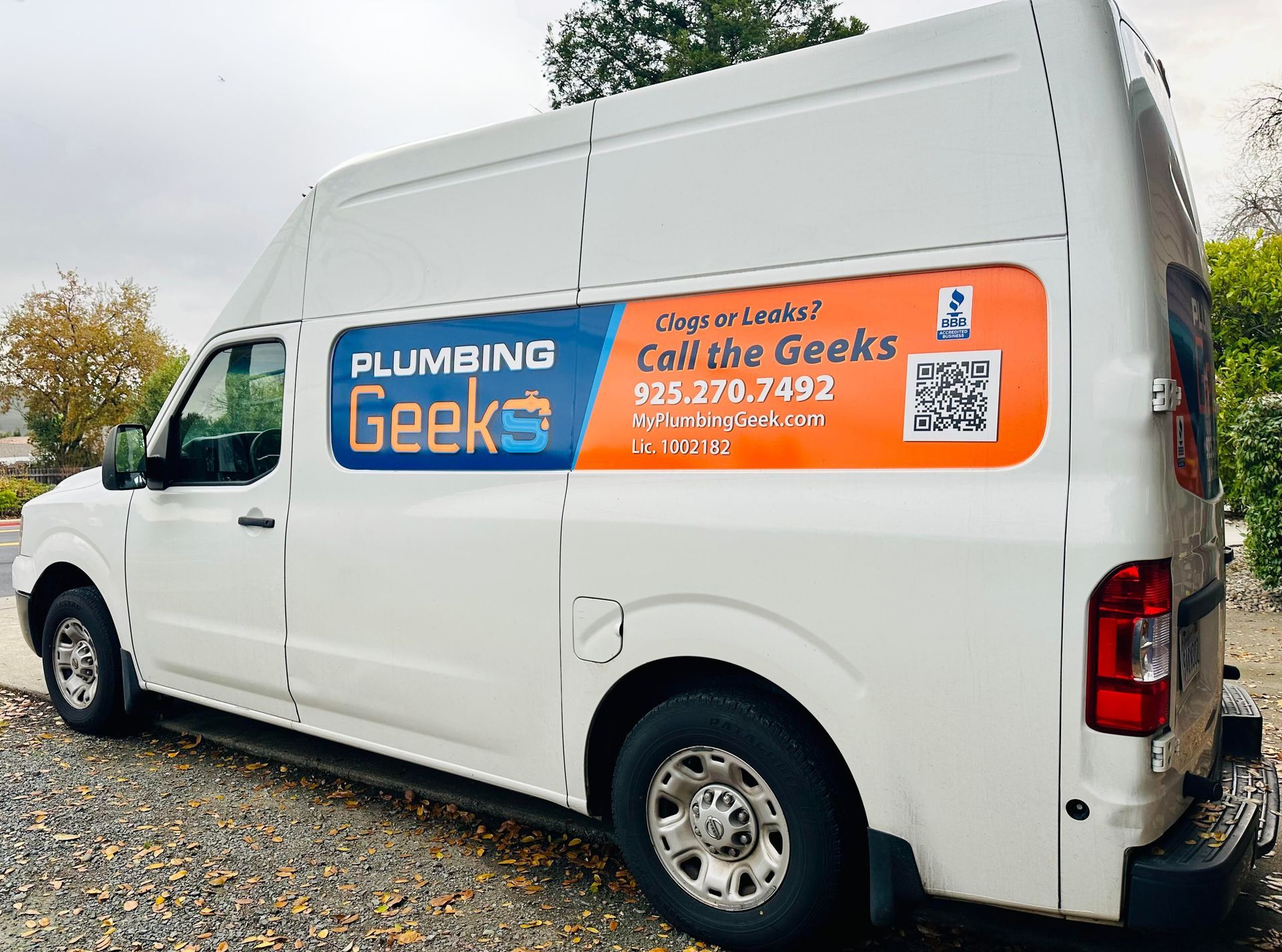 White Plumbing Geeks van parked on a gravel driveway, with business information on the side panel.