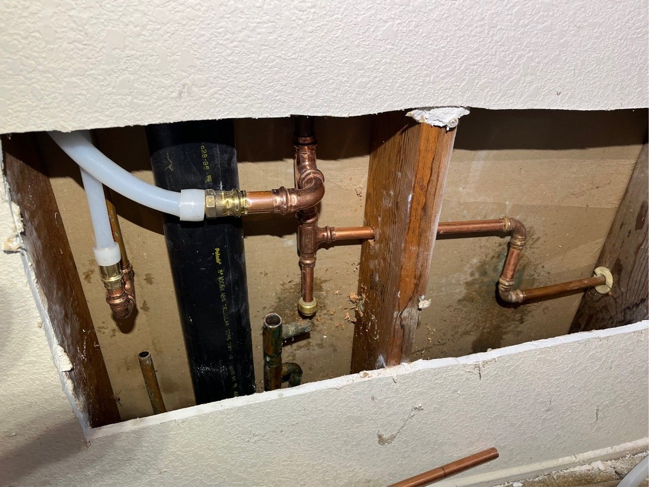 Copper plumbing pipes and PEX tubing in a wall cavity, with a black drain pipe visible.