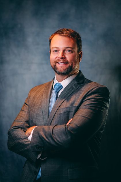 A man in a suit and tie is standing with his arms crossed.